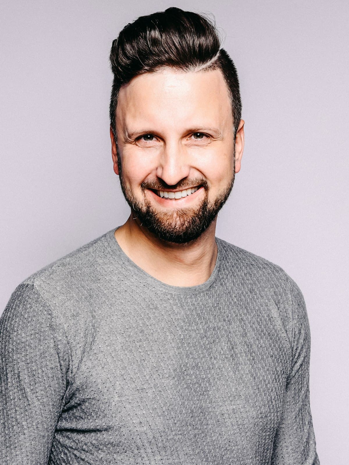 A man in a grey sweater smiling